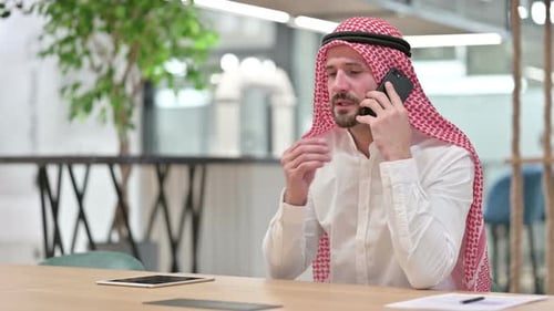 Man in Traditional Dress Talking on Phone at Desk