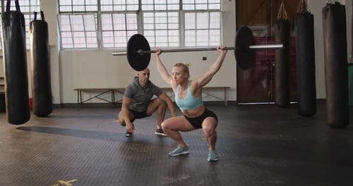 Fit caucasian woman working out with barbell with male trainer at the gym