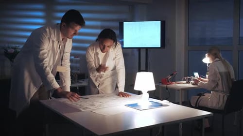 Elektronikingenieure gemischter Rassen in weißen Kitteln diskutieren im Labor über das Schema der Steuerelektronik