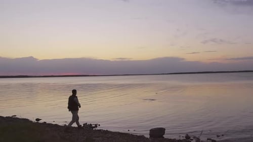 Man Skipping Stones at Sunset on Rocky Lake Shore