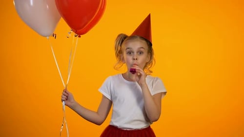 Nettes Mädchen mit Partygebläse, das Luftballons hält und Geburtstag feiert, Happy