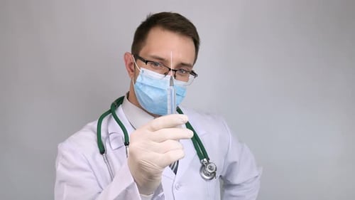 Doctor Holds up Medical Syringe Wearing Mask and Gloves