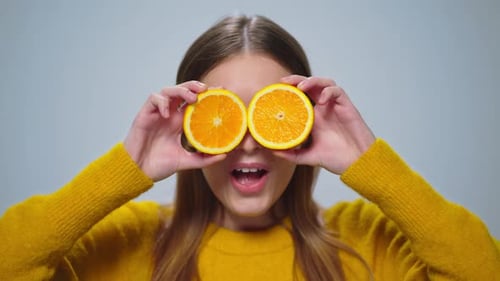Portrait of Cheerful Woman Having Fun with Two Orange Slices in Studio