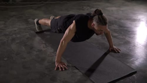Caucasian Man with Dreadlocks in Black Sportswear Does Pushups in Empty Gym or Studio