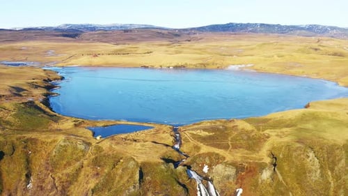 Aerial of a Little Blue Lake in Valley Surrounded with Golden Fields Iceland