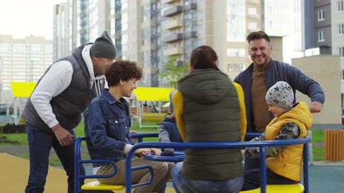 Two Happy Families Enjoying Roundabout Ride in Playground