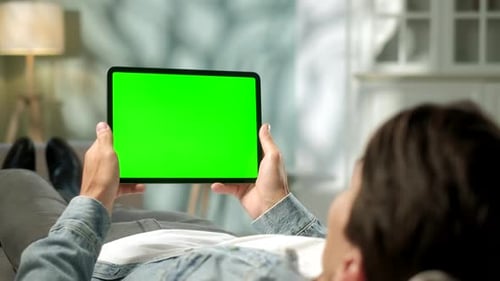 View From the Shoulder of Man Holding and Using Hand Gestures on Green Mock-up Screen Digital Tablet