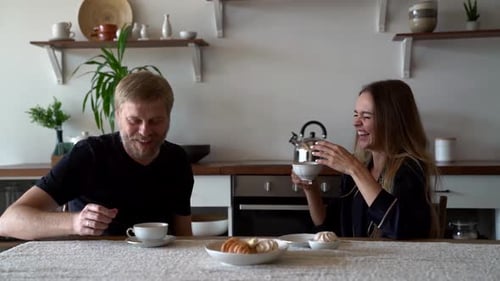 Laughing Couple Having Coffee and Croissants at Home