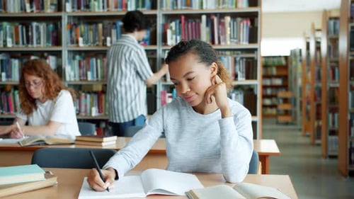 Mixed Race Student Studying in Library While Other People Learning in Background