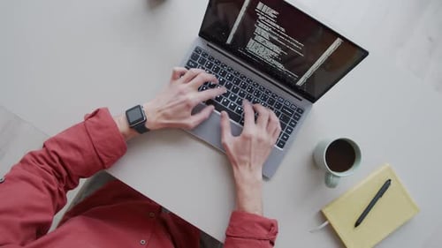 Programmer Typing Code on Laptop at Desk