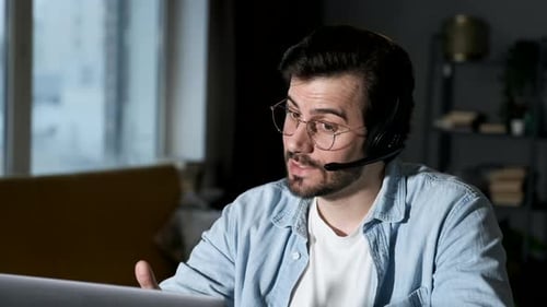 Close-Up of a Young Man Using a Laptop, Talking through a Headset, Chatting Online with Friends