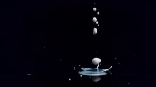 Gotas de leche sobre superficie negra sobre fondo negro. Cámara lenta.