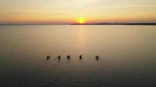 Cinco caiaques com pessoas navegando em direção ao nascer do sol