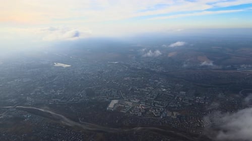 Aerial View From High Altitude of Distant City Covered with Puffy Cumulus Clouds Flying By Before