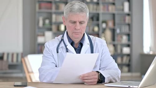Médecin professionnel d'âge moyen lisant des documents pendant qu'il est assis au bureau