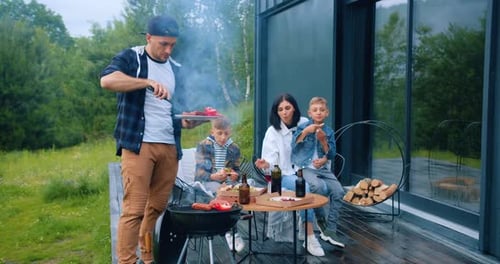 Dad Puts on the Grill Sausages and Vegetables, Cooking BBQ Party for His Family