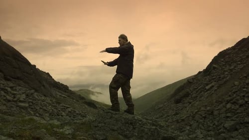 Young Guy Makes Smooth Movements with His Hands Standing on a Mountain Crossing