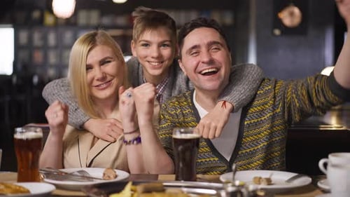 Front View Excited Caucasian Family Gesturing Victory Smiling Sitting in Restaurant Indoors