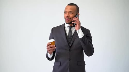 Professioneller afroamerikanischer Geschäftsmann hält eine Tasse Kaffee im Gespräch auf dem Handy