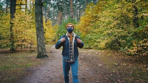 Slow Motion Shot of Young Male Tourist in Protective Mask Walking Alone in Autumn Forest