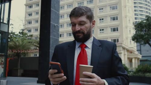 Man in Suit Using Smartphone Holding Coffee Outdoors