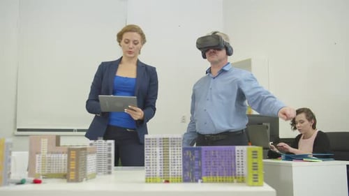 Architect with Tablet in Hands Tells Something To Her Colleague in Virtual Glasses in the Office