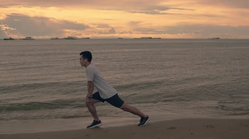 Athletic Young Adult Stretches on Beach at Sunrise