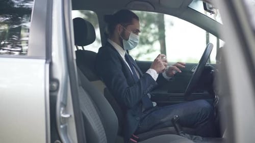 Man Using Hand Sanitizer in Car with Mask