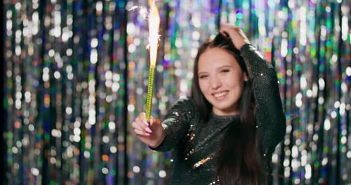 Woman Celebrates with Sparkler in Front of Tinsel Backdrop