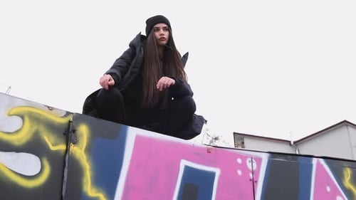 Stylish Woman Sits on Graffiti-Covered Structure