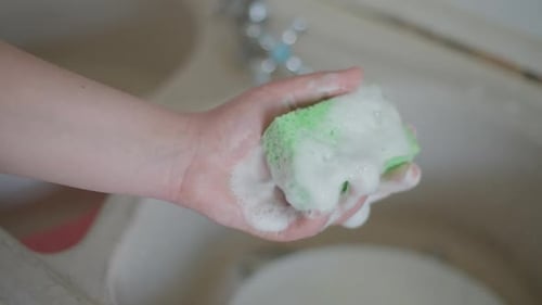 Hand Squeezing Bubbly Sponge in Sink