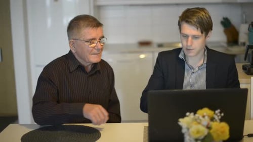 Joven enseñando a un hombre mayor cómo usar la computadora portátil en casa