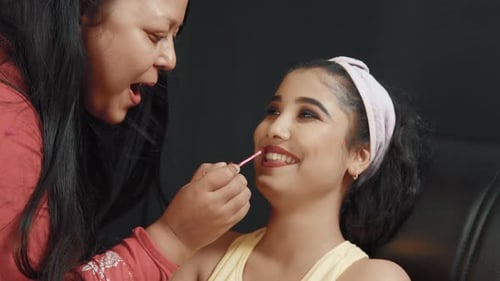 Close up of beautiful young woman in cosmetics studio and make up artist putting lipstick on her lip