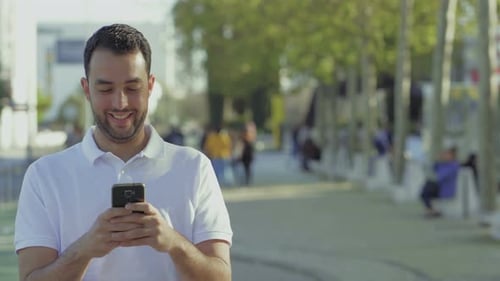 Smiling Man Uses Smartphone in Urban Environment