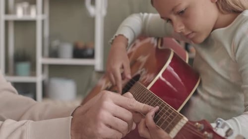 Girl Learning Guitar with Adult Indoors