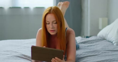 Woman with Tablet Relaxing on Bed Indoors