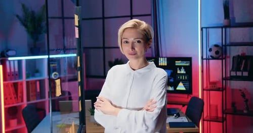 Femme d'affaires posant devant la caméra avec les bras croisés et l'expression faciale confiante dans un bureau en soirée