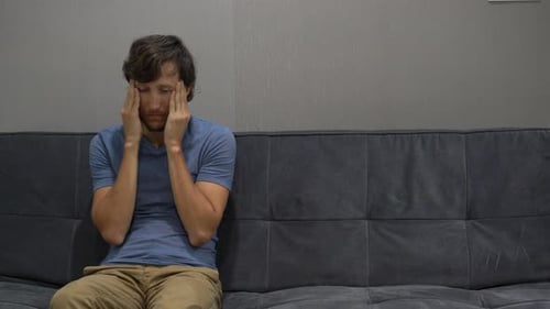 Ein junger Mann sitzt auf einer Couch und ein Mann fühlt sich verärgert und verwirrt. Space auf der rechten Seite kopieren