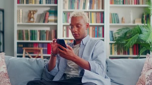 Smiling Young Adult Using Smartphone on Sofa