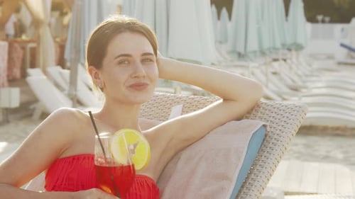 Lovely Young Woman Sipping Cocktail While Sunbathing at the Beach