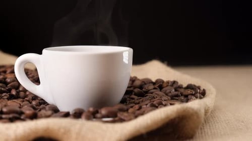 Cup of Steaming Coffee on Burlap With Beans