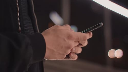 Detail shot with hands of a man writing-texting a message on the phone in the city at night