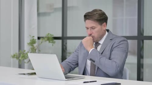 Middle Aged Man Coughing while using Laptop in Office