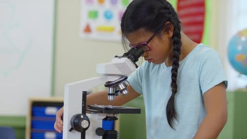 Young girl in school classroom looking into microscope