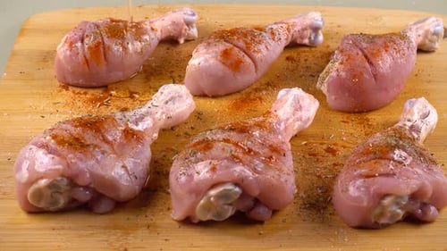 Hähnchenschenkel werden auf einem Schneidebrett mit Olivenöl bestreut. Der Prozess des Marinierens von Fleisch.