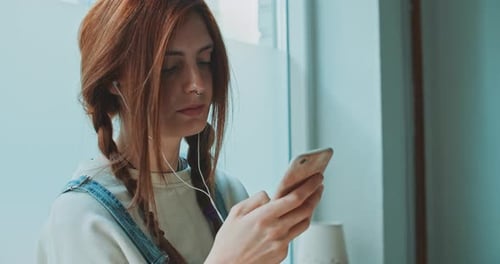 Woman Using Smartphone with Earbuds at Home