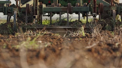 Tractor cultivating a green field in slow motion.