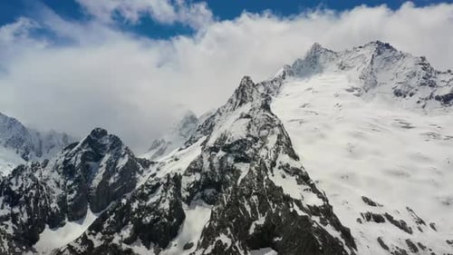Air Flight Through Mountain Clouds Over Beautiful Snowcapped Peaks of Mountains and Glaciers