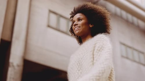 Smiling Young Woman With Windswept Afro Hair Walking Along Street