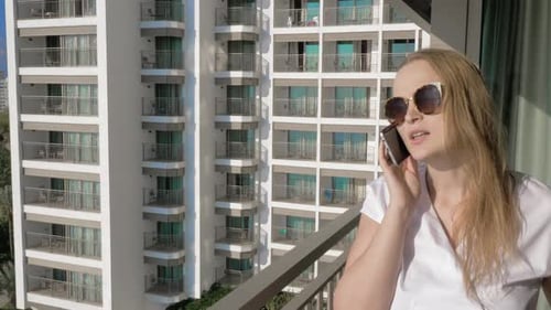 Woman Chatting on Cellphone on Balcony in City